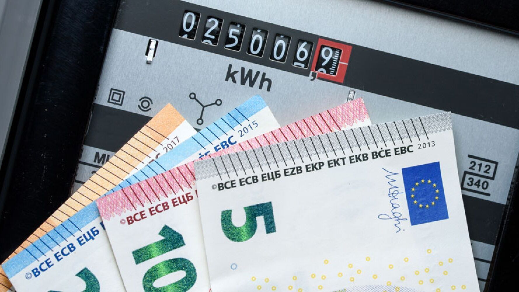 Abgebildet ist ein Stromzähler, davor werden verschiedene Geldscheine gehalten.