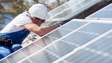 Zu sehen ist ein Mann, der eine Solaranlage auf einem Dach wartet. 