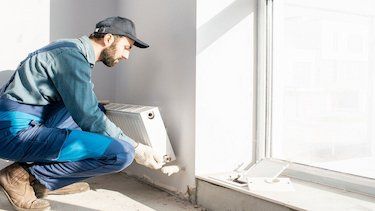 Ein Handwerker montiert einen Heizkörper an einer Wand. 