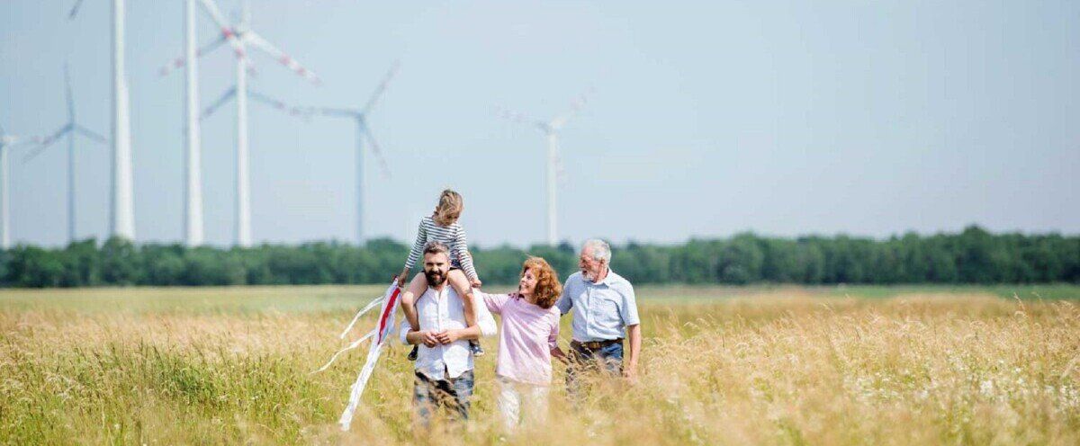 Eine Familie läuft über ein Feld mit Windrädern im Hintergrund, die Windenergie erzeugen.