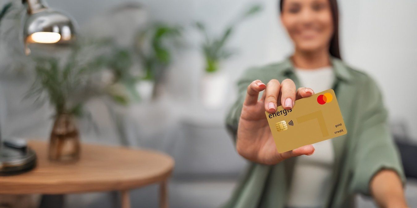 Frau hält energis Mastercard GOLD in die Kamera und sitzt in ihrem Wohnzimmer