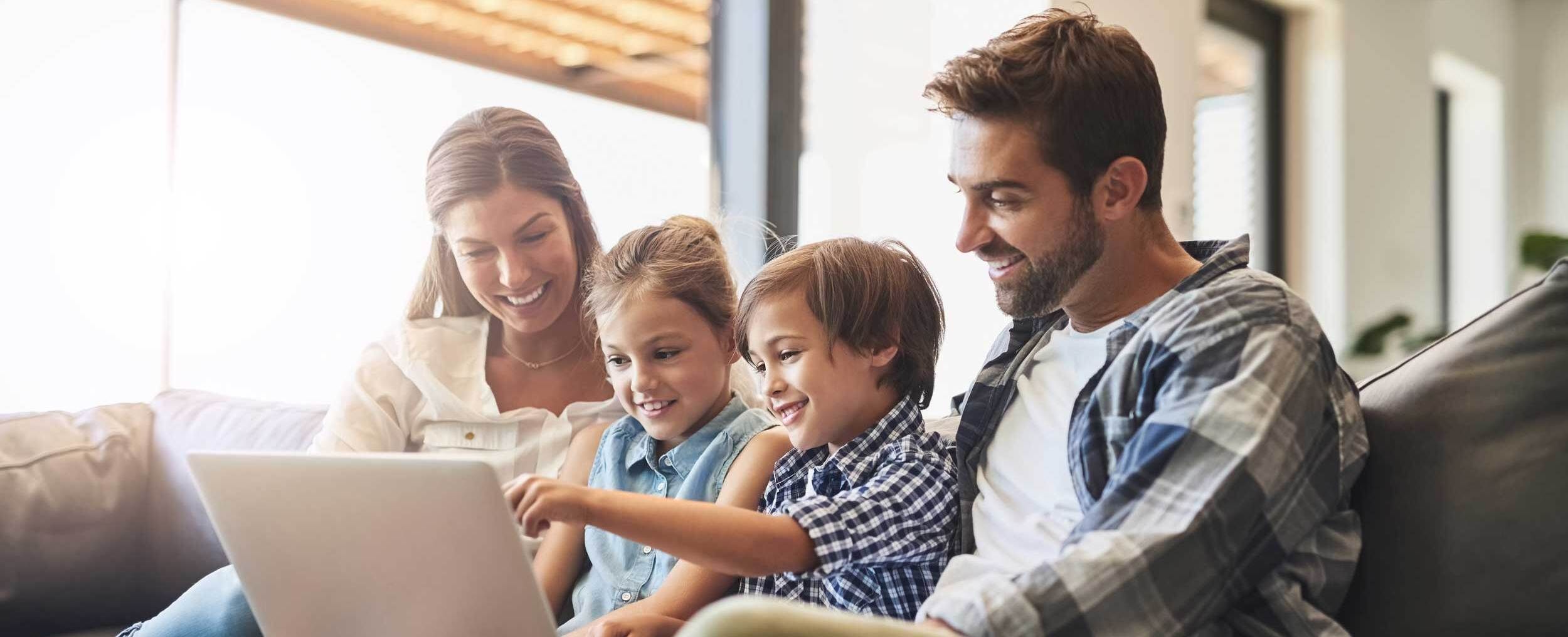Familie sitzt auf dem Sofa mit Laptop.