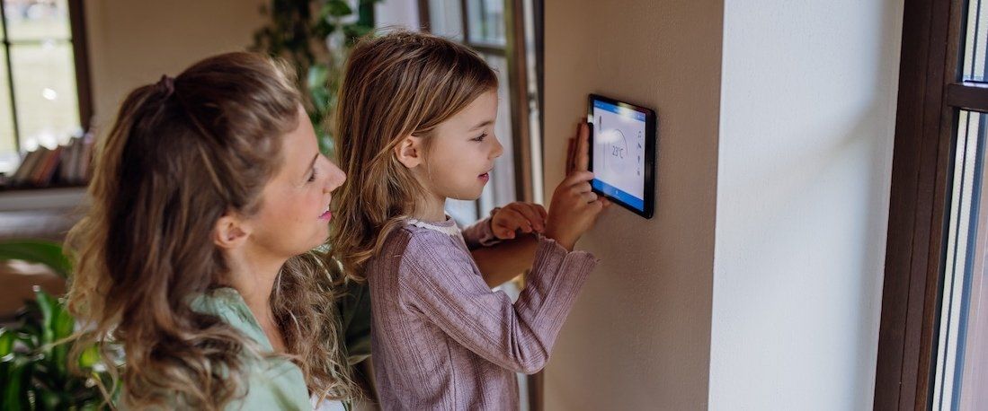 Frau und Kind bedienen gemeinsam eine digitale Heizungssteuerung an der Wand.