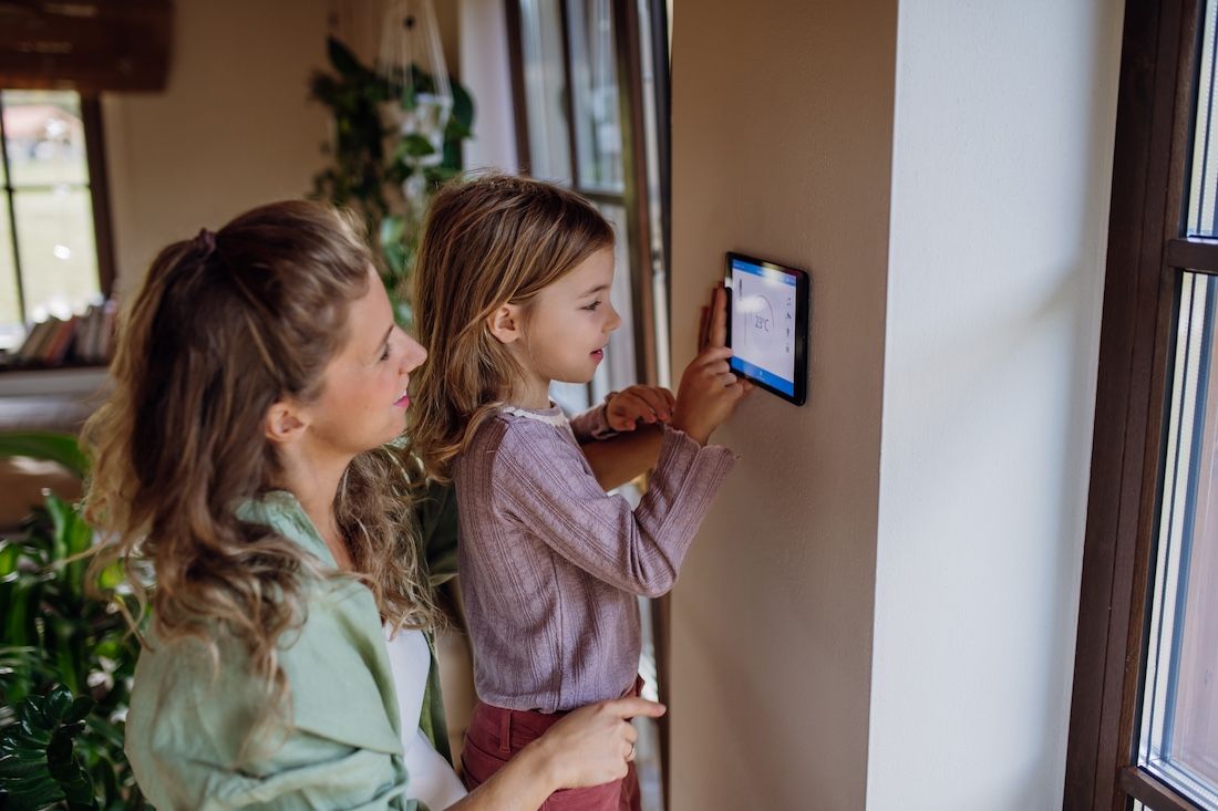 Frau und Kind bedienen gemeinsam eine digitale Heizungssteuerung an der Wand.