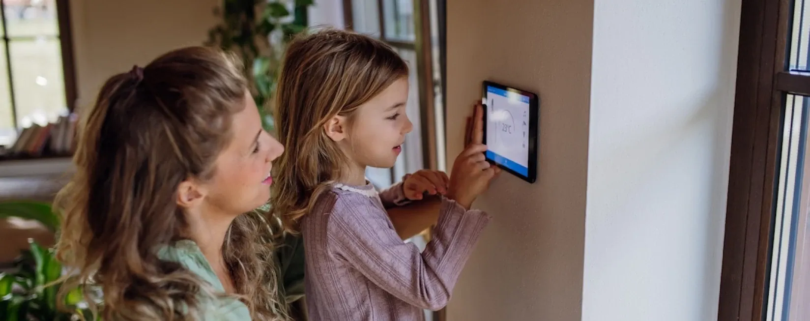 Frau und Kind bedienen gemeinsam eine digitale Heizungssteuerung an der Wand.